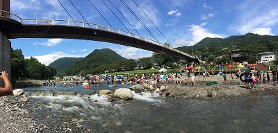 青い空と川に掛かる橋の下でにぎわう人たち